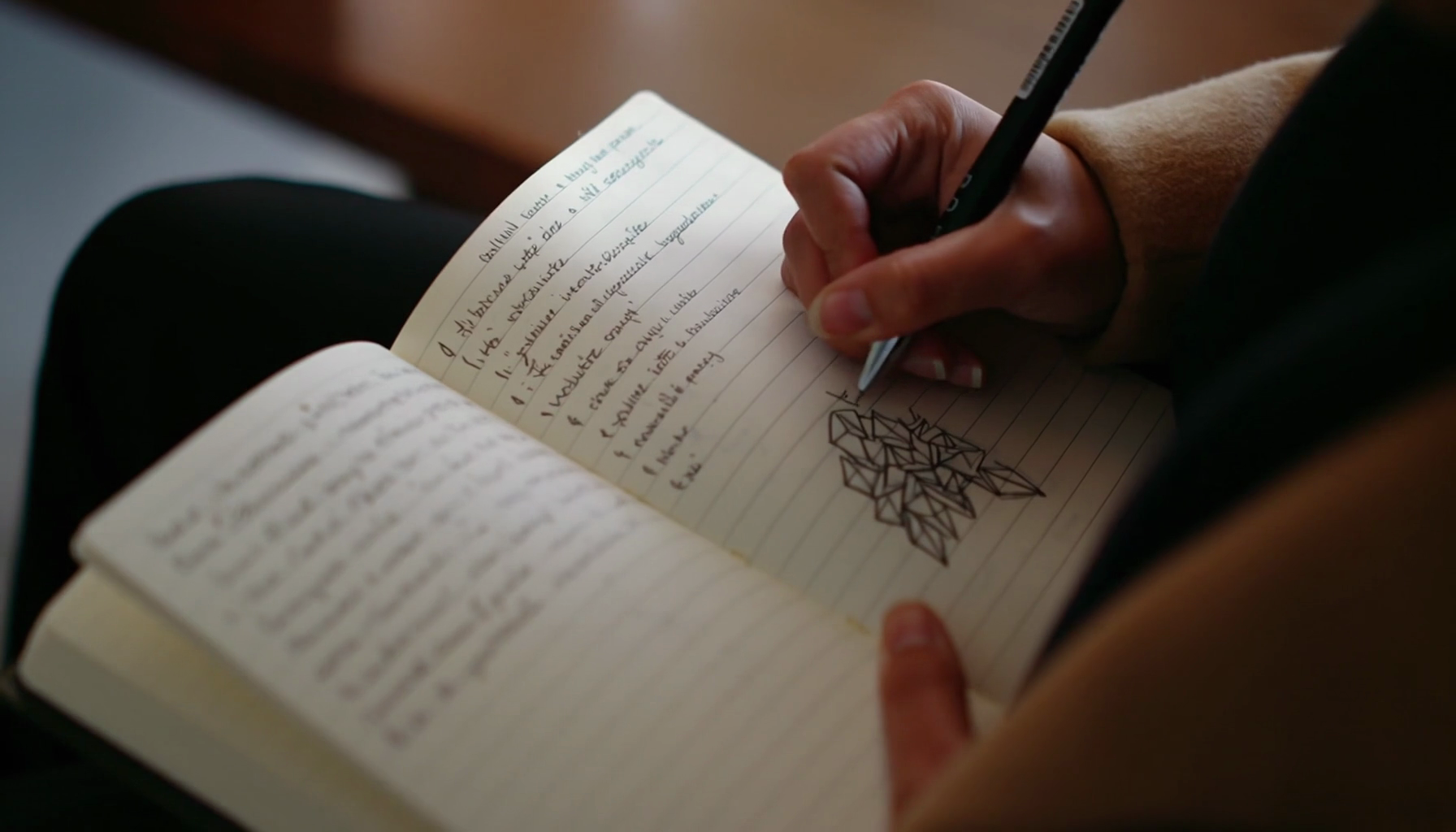 Eine Hand schreibt mit Stift in ein liniertes Notizbuch, daneben eine geometrische Skizze